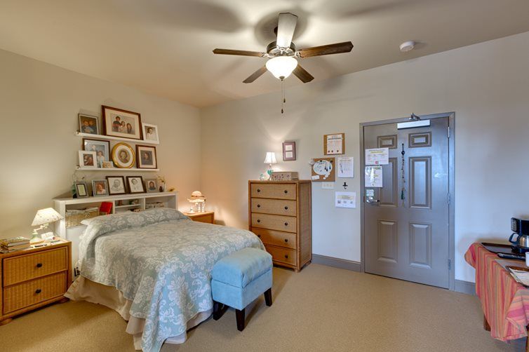 A cozy bedroom with a comfortable bed, wooden dresser, and ceiling fan, decorated with various framed artworks.
