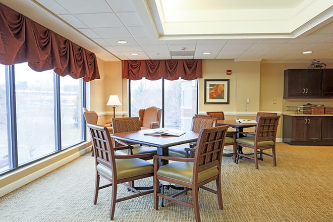 A cozy dining area with tables and chairs, well-lit by large windows.