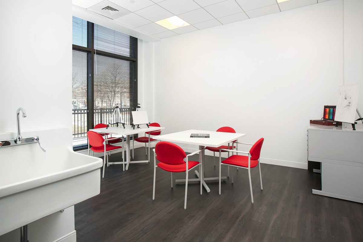 A modern meeting room with a conference table surrounded by red chairs and illuminated by natural light from a large window.