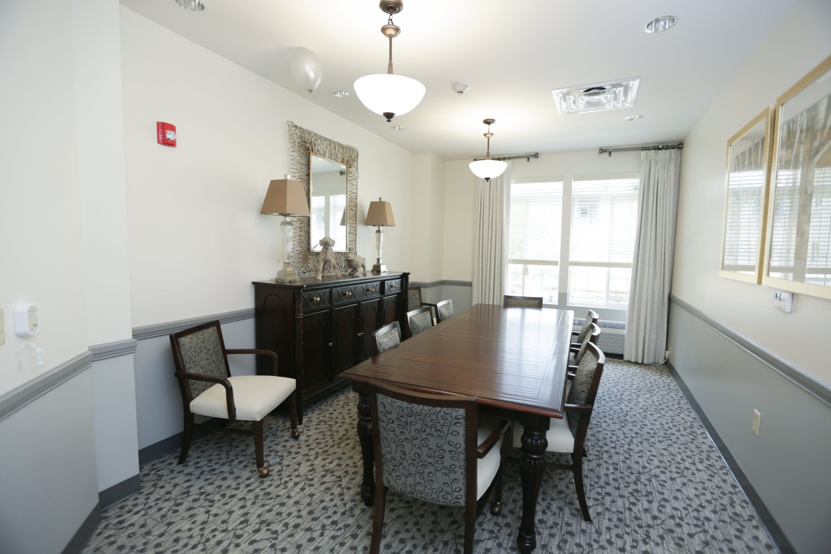 A well-lit dining room with a long wooden table, upholstered chairs, and elegant decor.