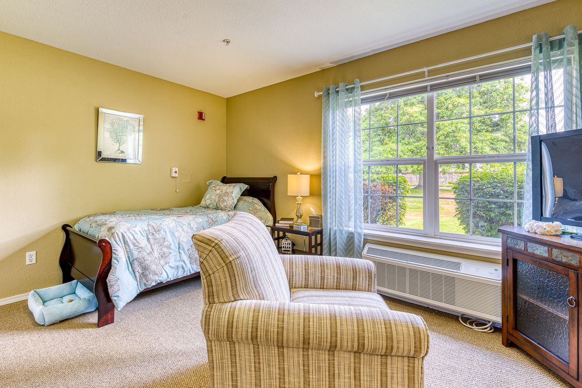 A cozy bedroom with a bed, armchair, and a large window allowing natural light to fill the room.
