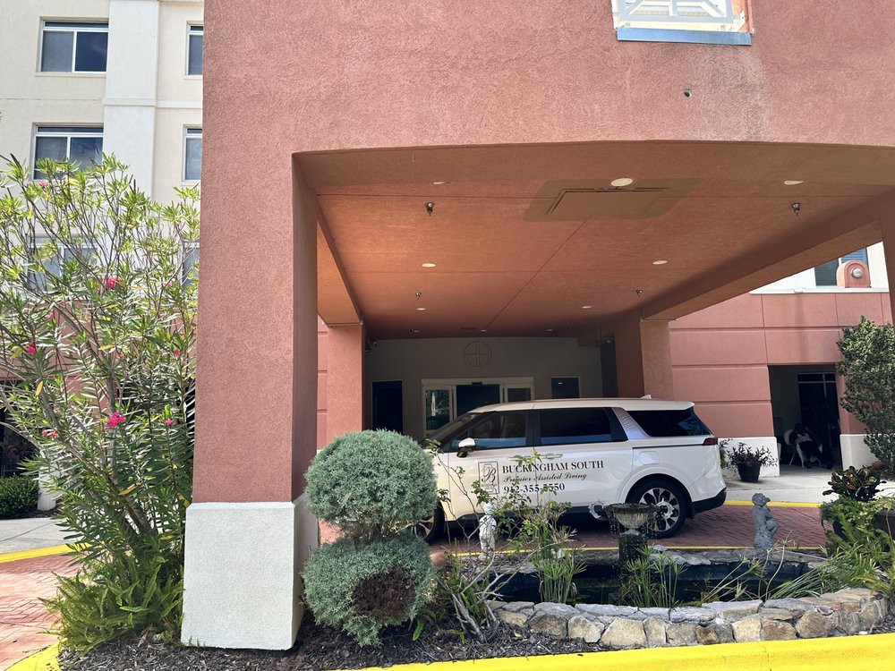 A hotel entrance with a vehicle parked under the carport surrounded by landscaping.