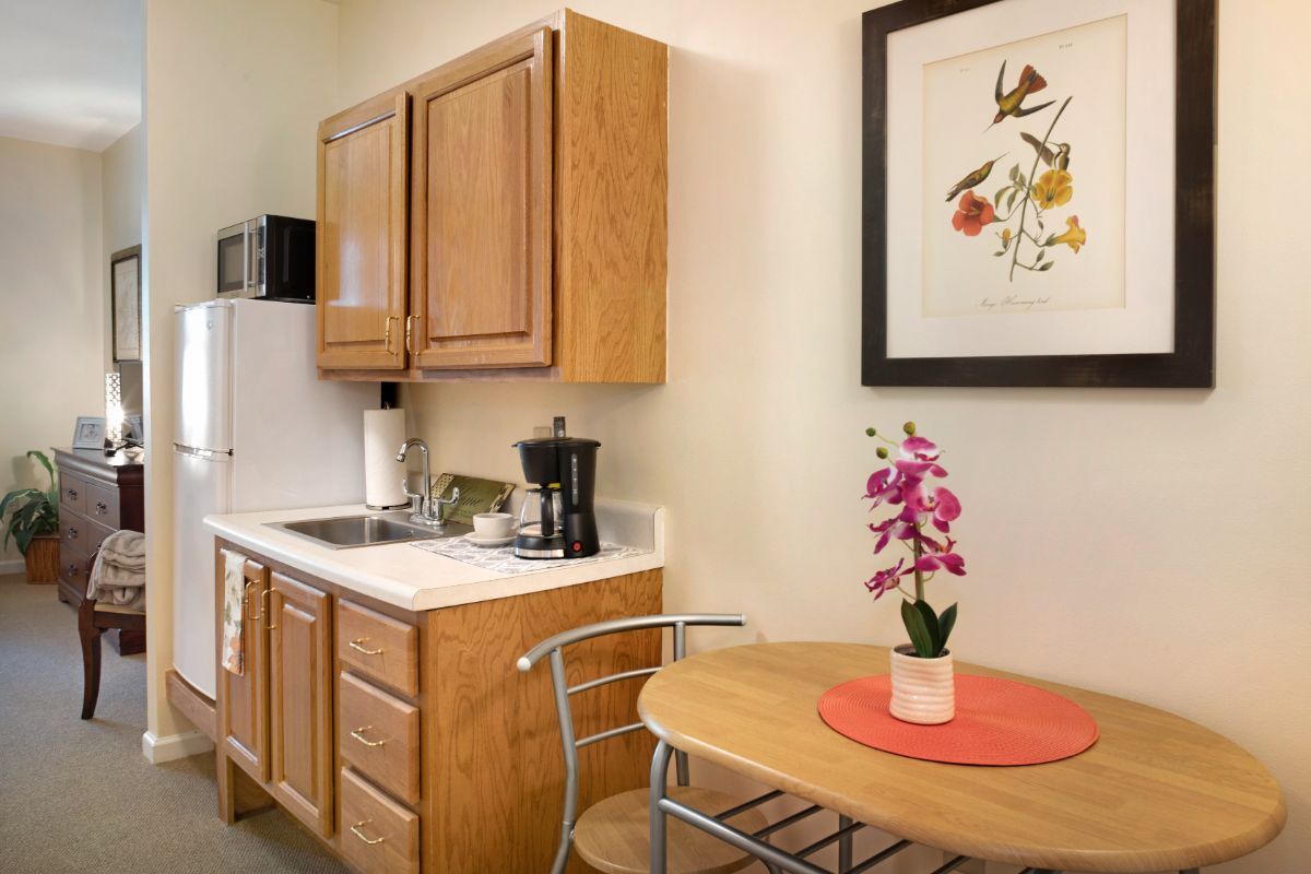 A cozy kitchen area with wooden cabinets, a small table with an orchid centerpiece, and framed artwork on the wall.