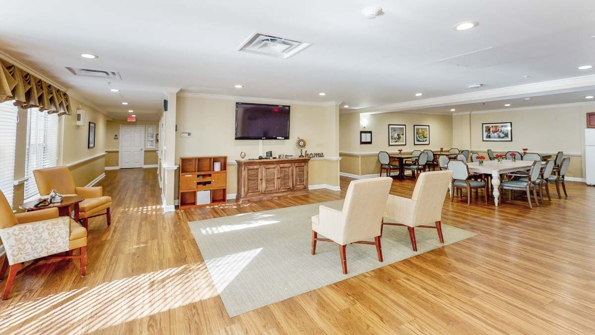 A spacious room with hardwood floors, featuring comfortable chairs and a mounted television.