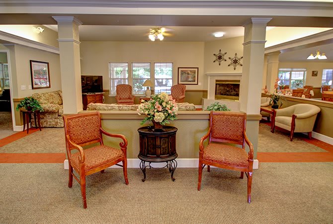 A cozy living room with two chairs, a small table adorned with flowers, and a fireplace in the background.