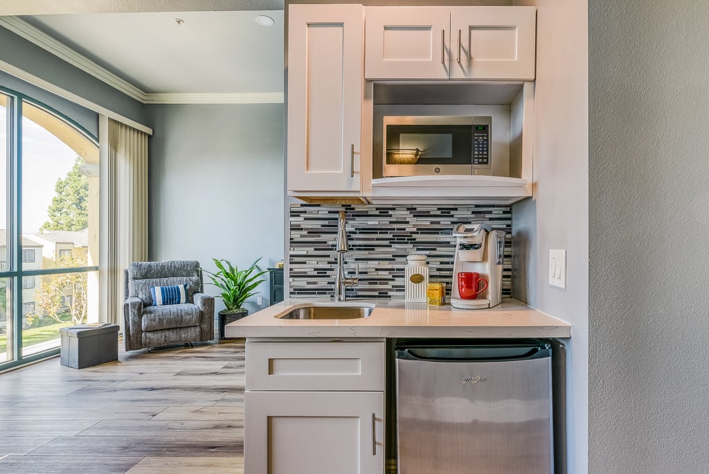 A modern and compact kitchenette featuring a microwave, sink, and small refrigerator with stylish cabinetry and backsplash.