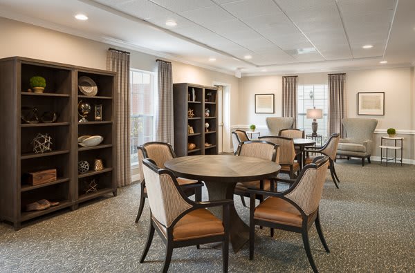 A cozy dining room with round tables, cushioned chairs, and decorative bookshelves.