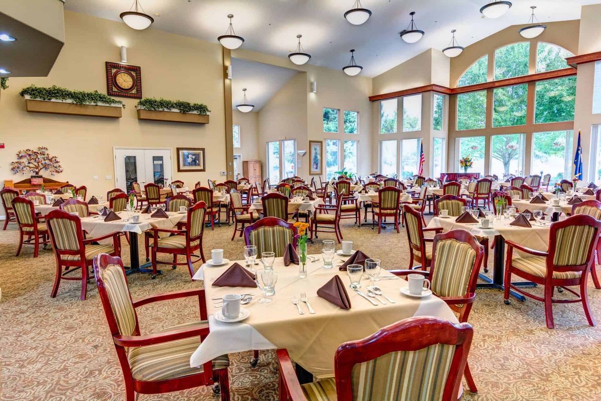 An elegant dining room with neatly arranged tables and chairs, filled with natural light from large windows.