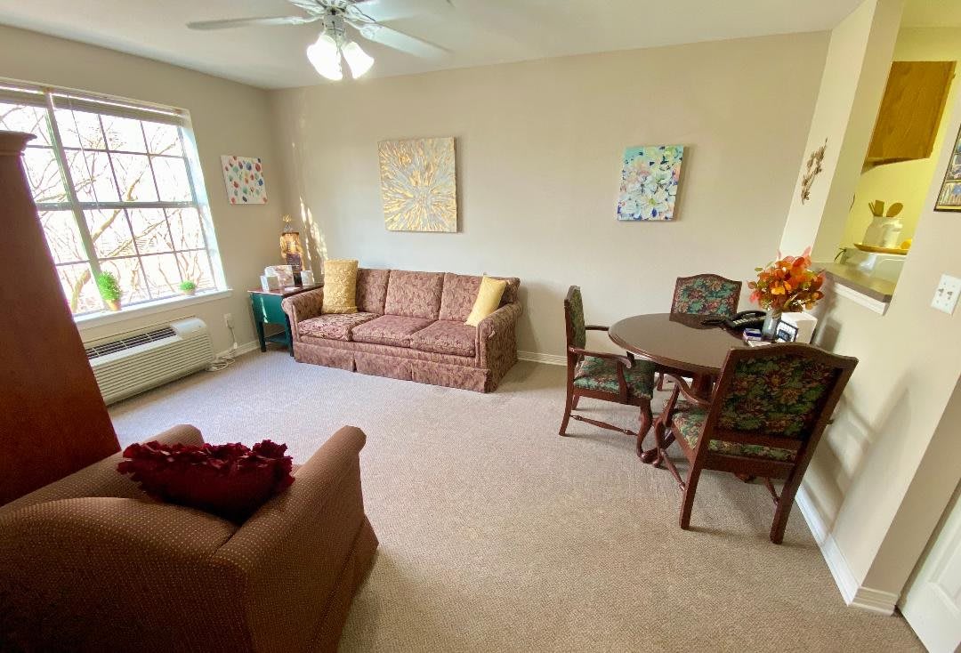 A cozy living room with a sofa, armchair, and dining table set under a ceiling fan.