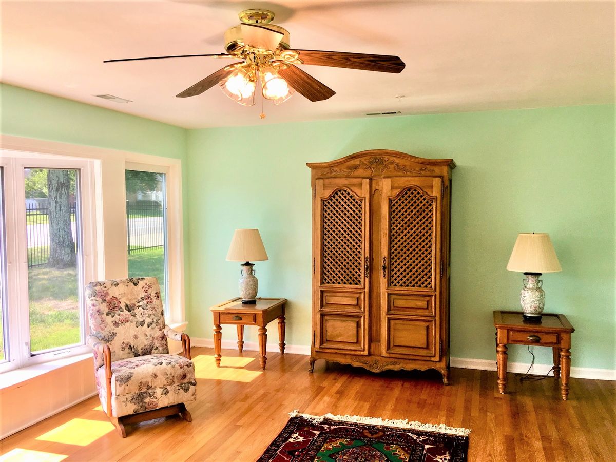 A cozy living room with an armoire, side tables, lamps, and a ceiling fan.