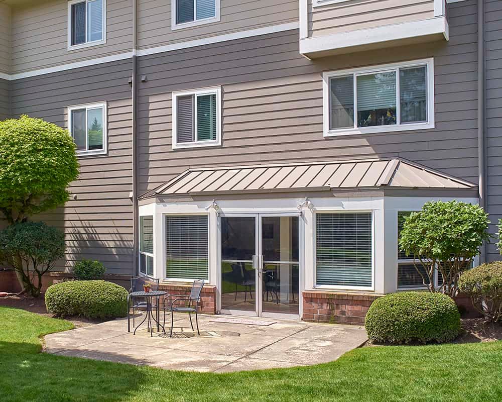 A modern house exterior with a patio, surrounded by greenery and equipped with outdoor furniture.