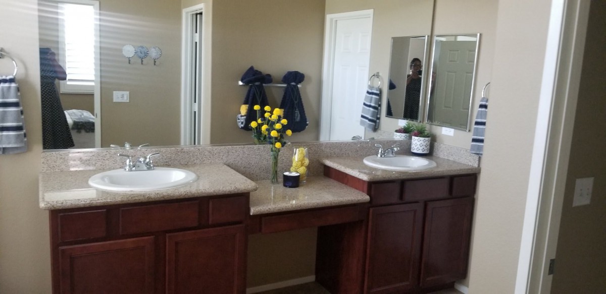 A bathroom featuring a double vanity with mirrors, decorated with yellow flowers and neatly hung towels.