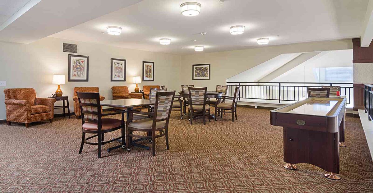 A cozy dining area with tables and chairs, carpeted flooring, and soft lighting.