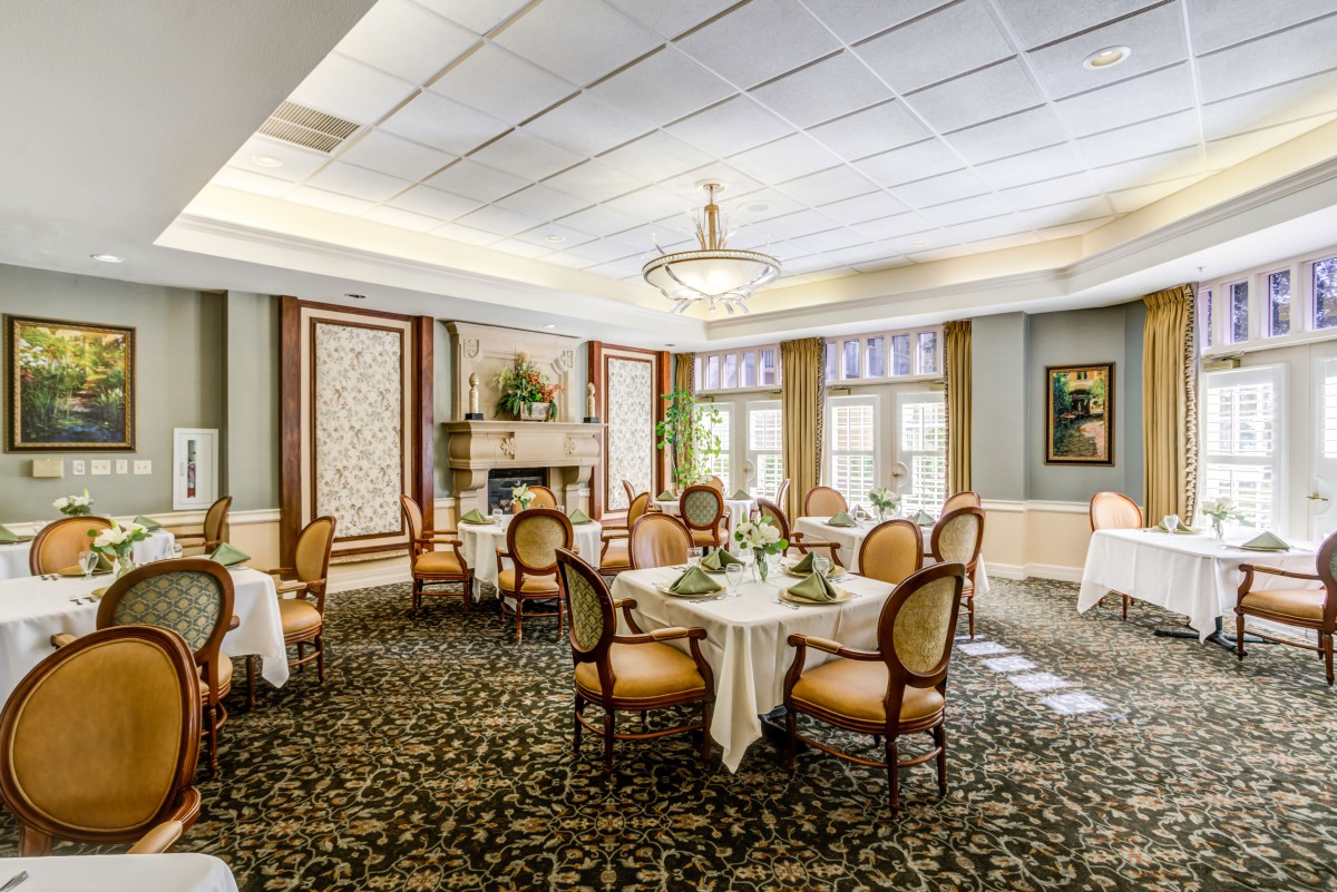 An elegantly designed dining room with round tables and upholstered chairs, featuring chandeliers and decorative carpeting.