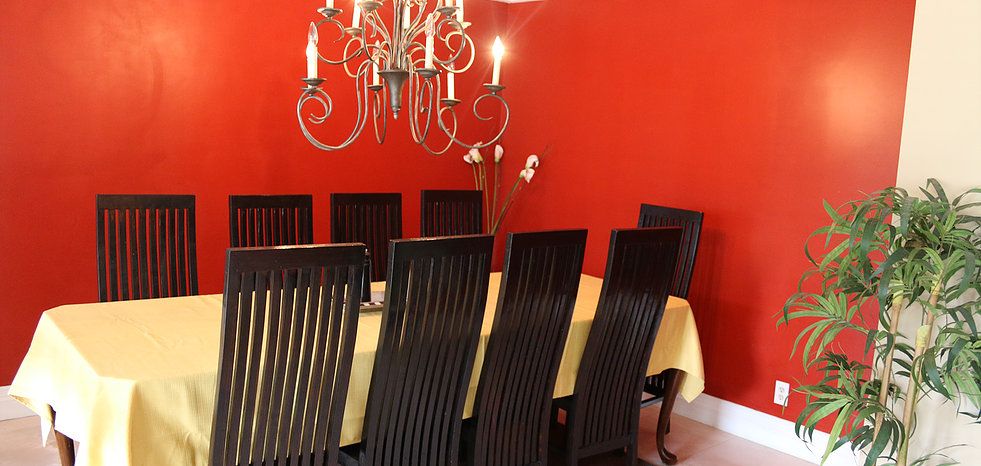A dining room featuring a chandelier, red walls, and a set of dark wooden chairs around a table.