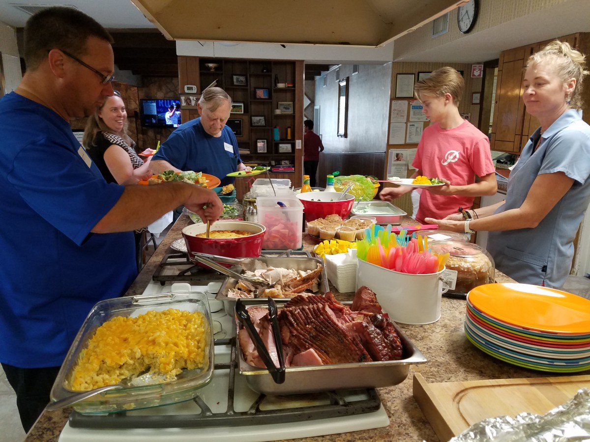 A group of people serving themselves food from a buffet table at an indoor gathering.