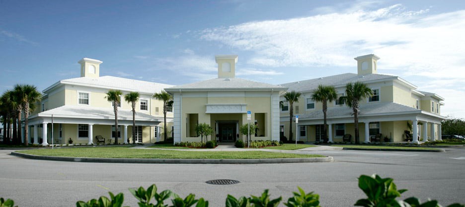 A modern building with palm trees and a central entrance under a clear sky.