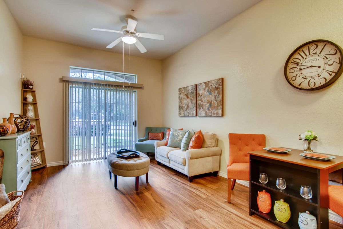 A cozy living room with a sofa, armchair, and coffee table, featuring a ceiling fan and sliding glass doors to an outdoor area.