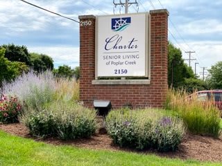 Outdoor sign for Charter Senior Living of Poplar Creek surrounded by greenery.