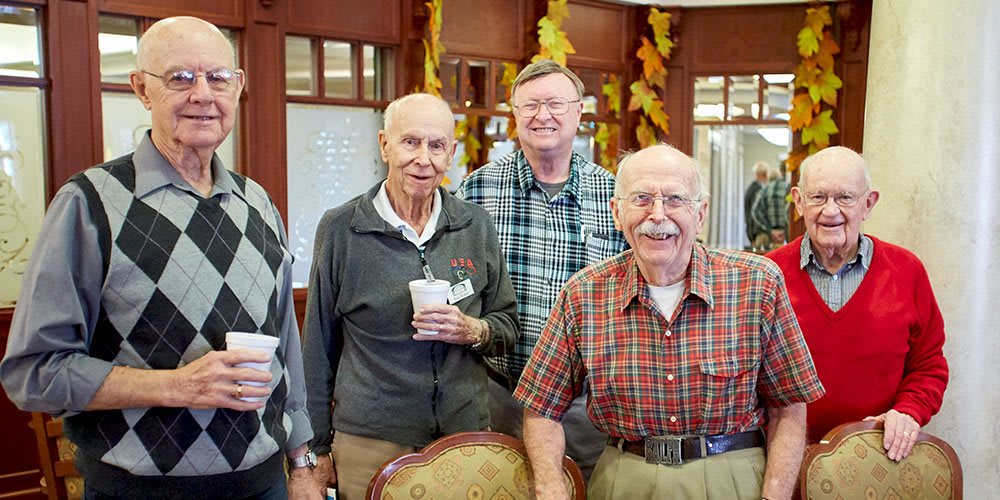 A group of elderly men smiling and enjoying a gathering indoors.