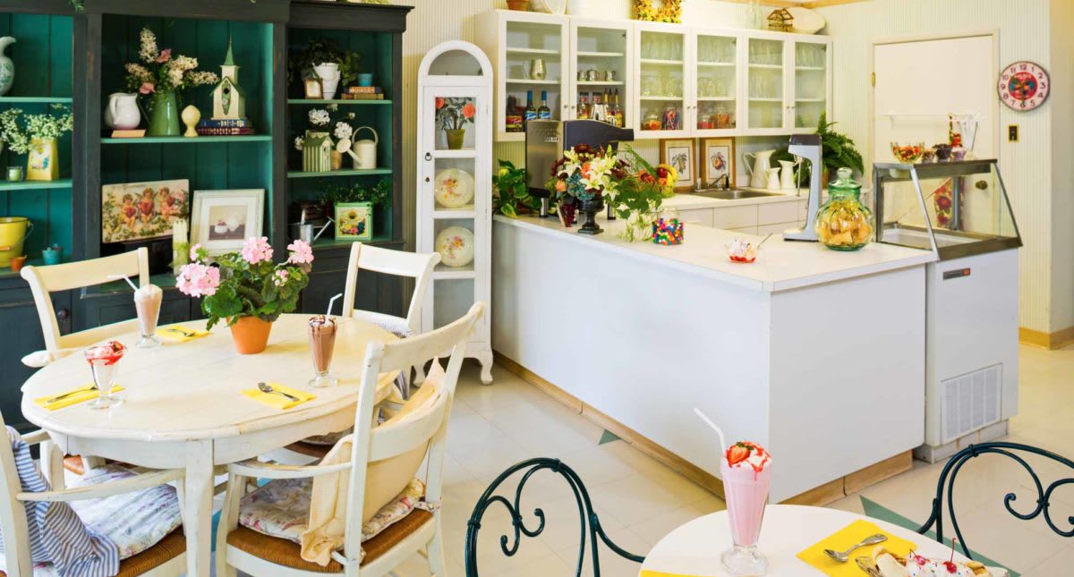 A quaint cafe interior with vintage decor, showcasing tables, chairs, and colorful floral arrangements.