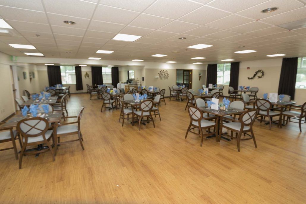 An empty dining hall with neatly arranged tables and chairs on a wooden floor.