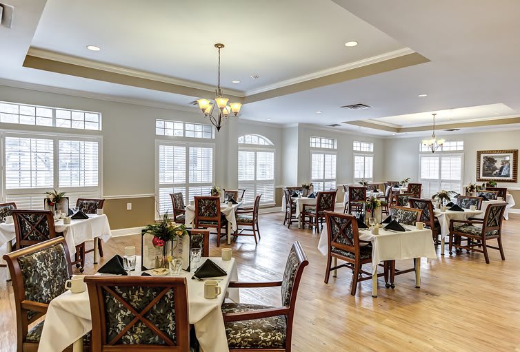 An elegant dining room with beautifully arranged tables and chairs, illuminated by natural light from large windows.