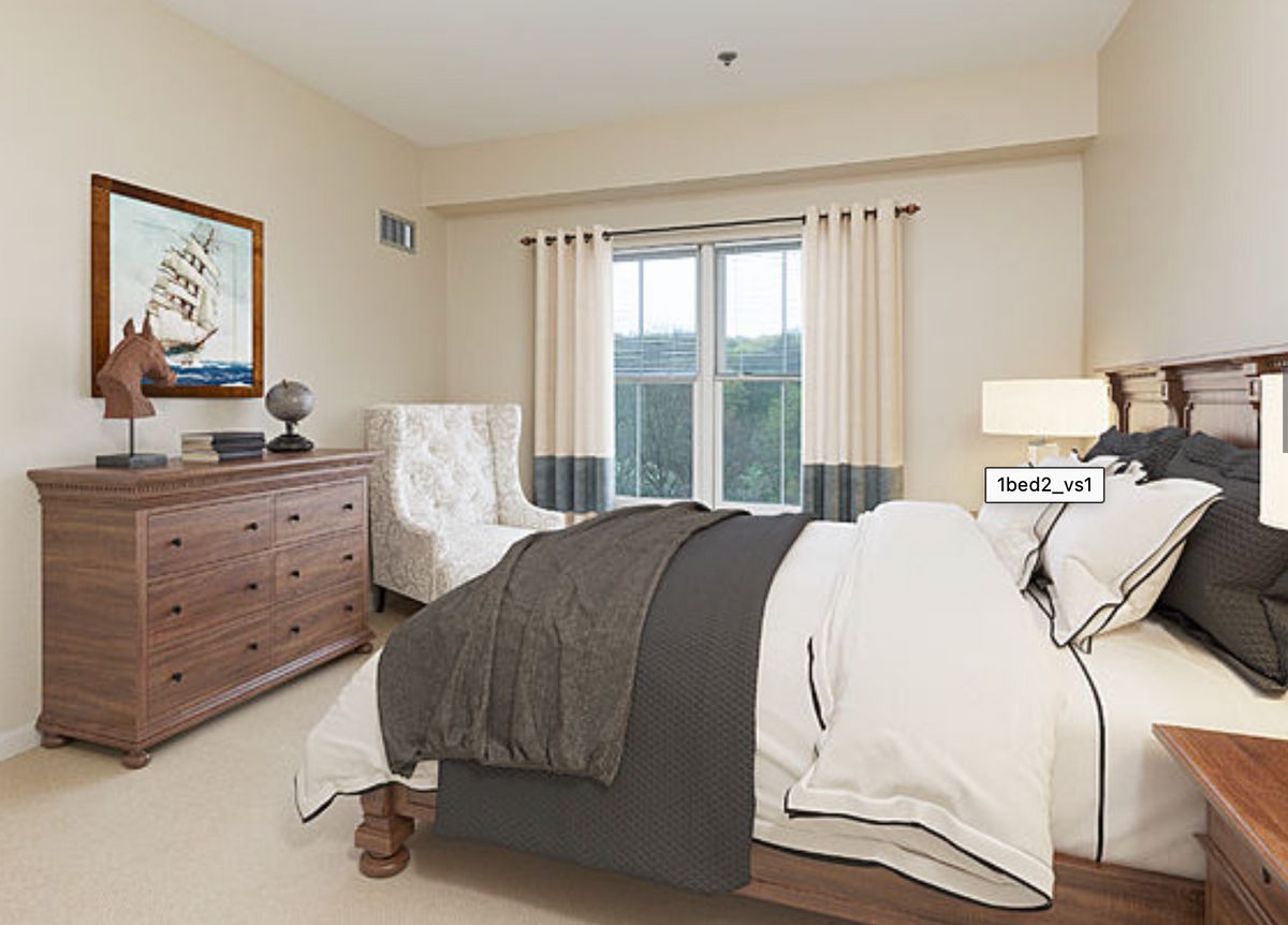 A cozy bedroom with a neatly made bed, wooden dresser, and a comfortable armchair by the window.