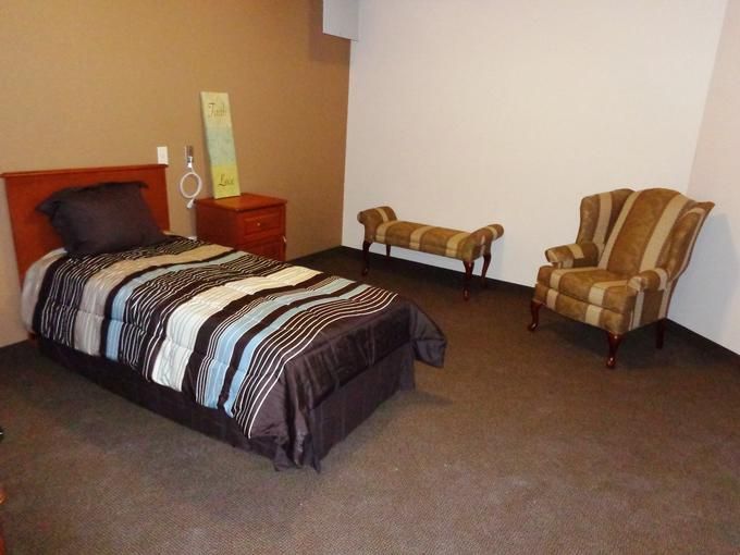 A minimalist bedroom with a single bed, striped bedding, and simple furnishings.
