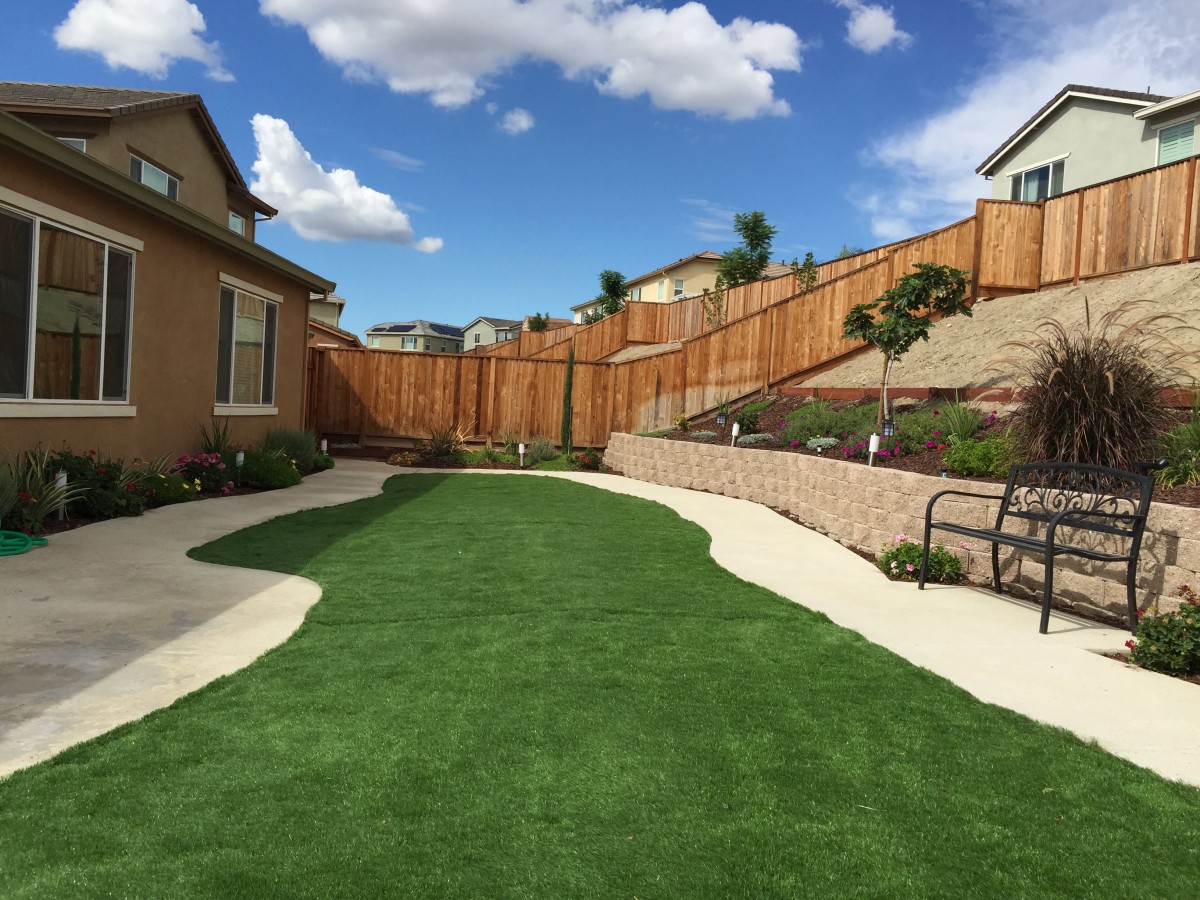 A well-maintained suburban backyard featuring artificial grass and a wooden fence.
