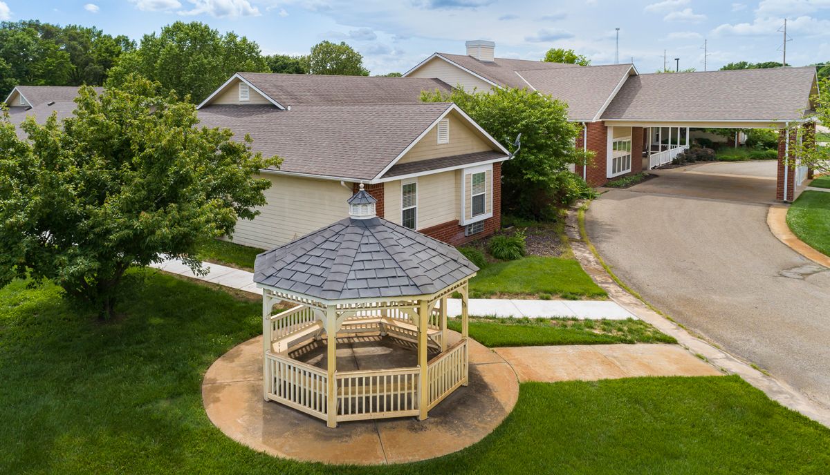 A peaceful outdoor setting with a wooden gazebo surrounded by houses and greenery.