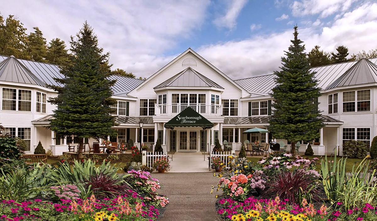 A charming white building with a welcoming entrance, surrounded by vibrant flowers and lush trees under a partly cloudy sky.