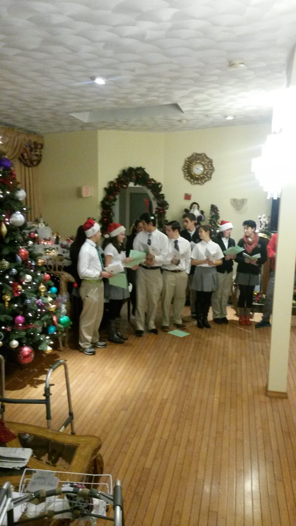 A group of people singing Christmas carols next to a decorated tree in a festive setting.