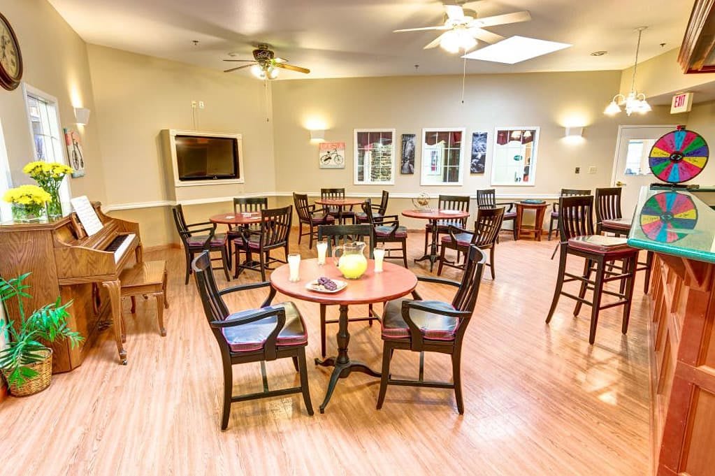 A cozy dining area with chairs and tables arranged neatly, featuring a wooden floor and overhead lighting.