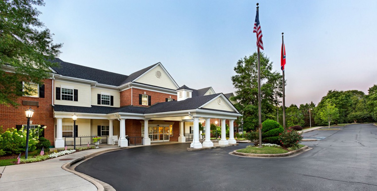 A hotel entrance with a driveway, columns, and surrounding greenery.