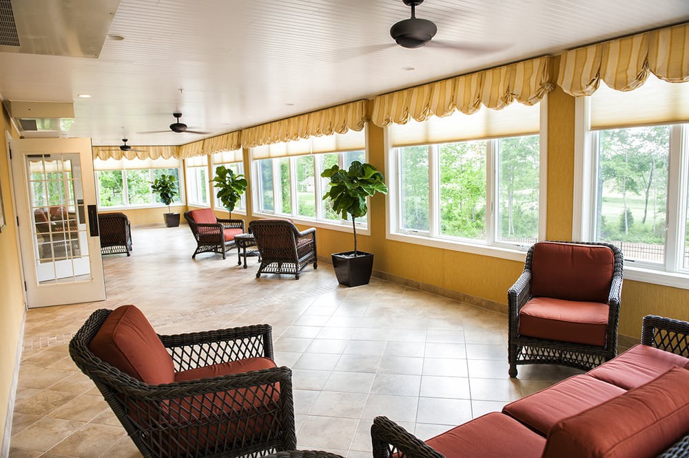A bright sunroom with wicker furniture, large windows, and ceiling fans.