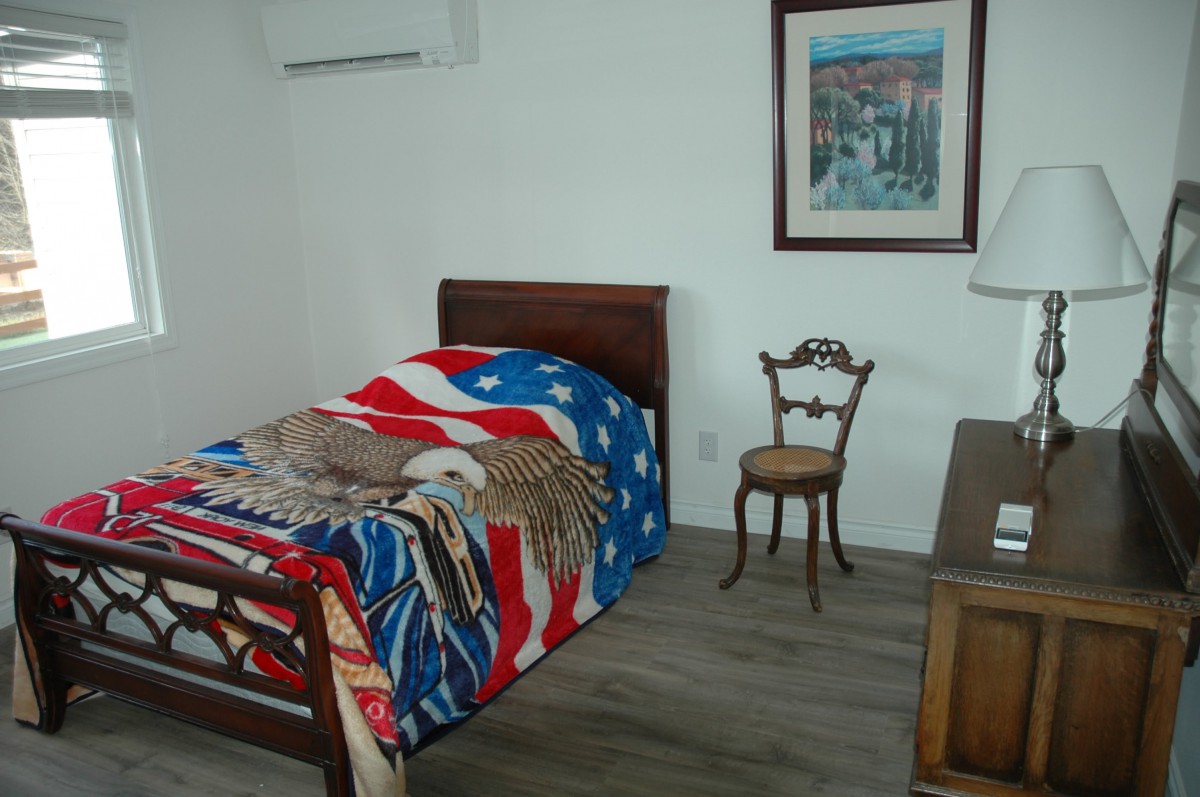 A minimalist bedroom with a single bed adorned with a star-patterned blanket, a decorative chair, and a framed painting on the wall.
