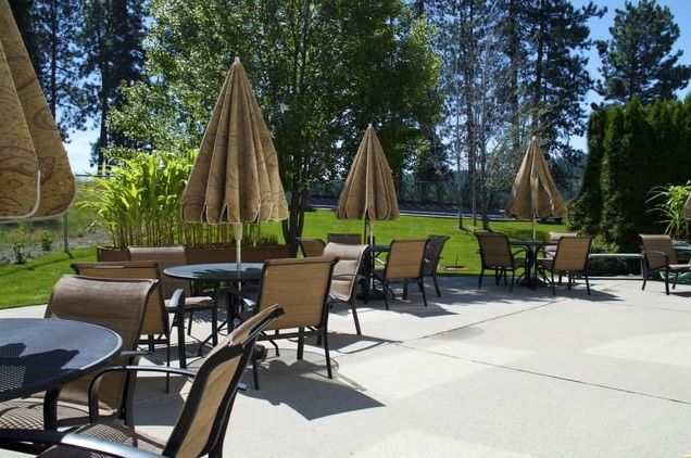 A sunny outdoor patio area with tables, chairs, and umbrellas.