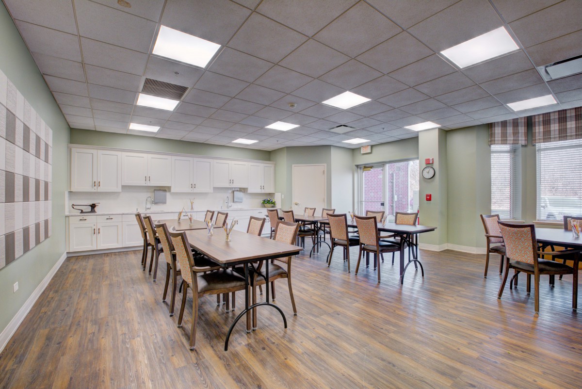 Spacious dining area with multiple tables and chairs, featuring a wooden floor and adjacent kitchen space.