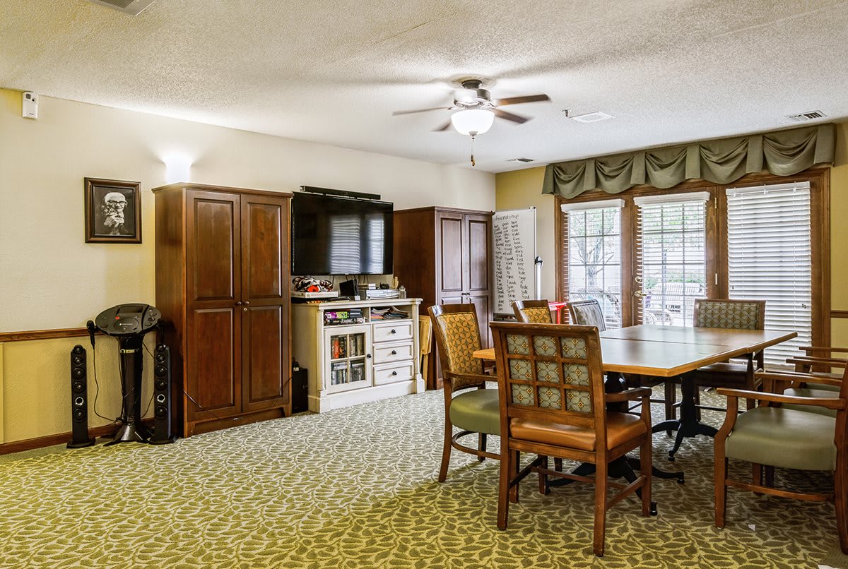 A cozy living and dining area with a carpeted floor, wooden furniture, and large windows.