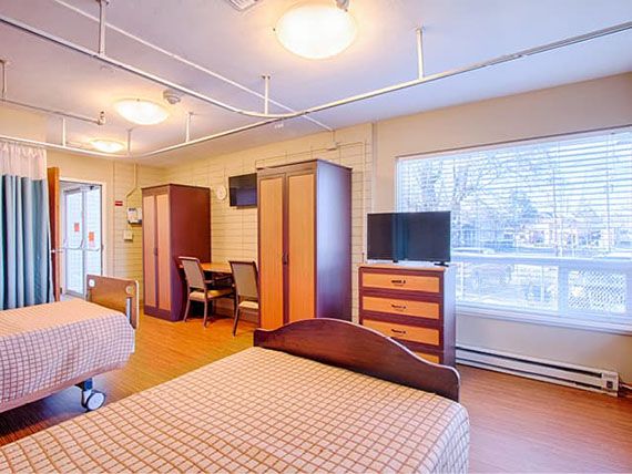 A spacious hospital room with two beds, wardrobes, and a television.