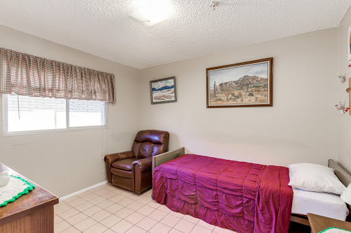 A cozy bedroom featuring a single bed with a maroon cover, a recliner chair, and framed artwork on the walls.