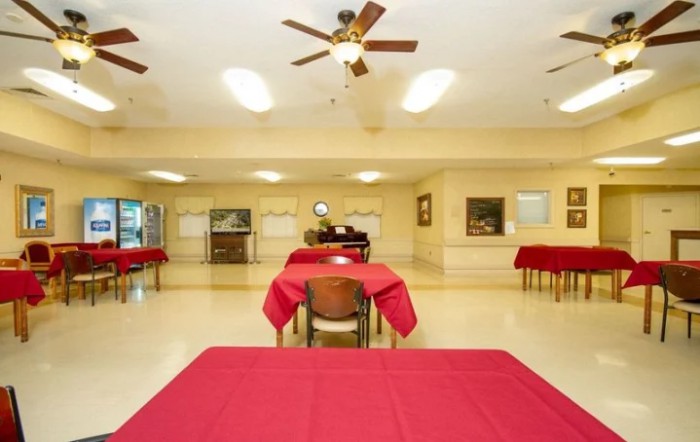 A spacious dining area with red tablecloth-covered tables and ceiling fans.
