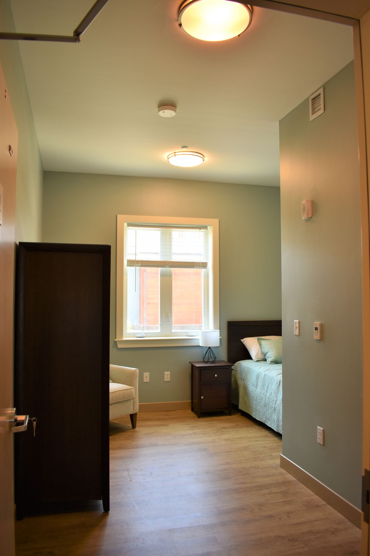 A cozy bedroom with a bed, nightstand, and armchair by the window.