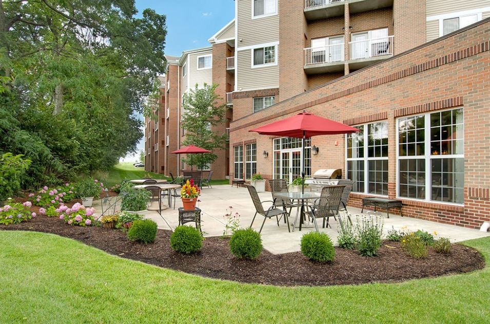 A well-maintained patio area with outdoor seating and red umbrellas in front of a residential building.