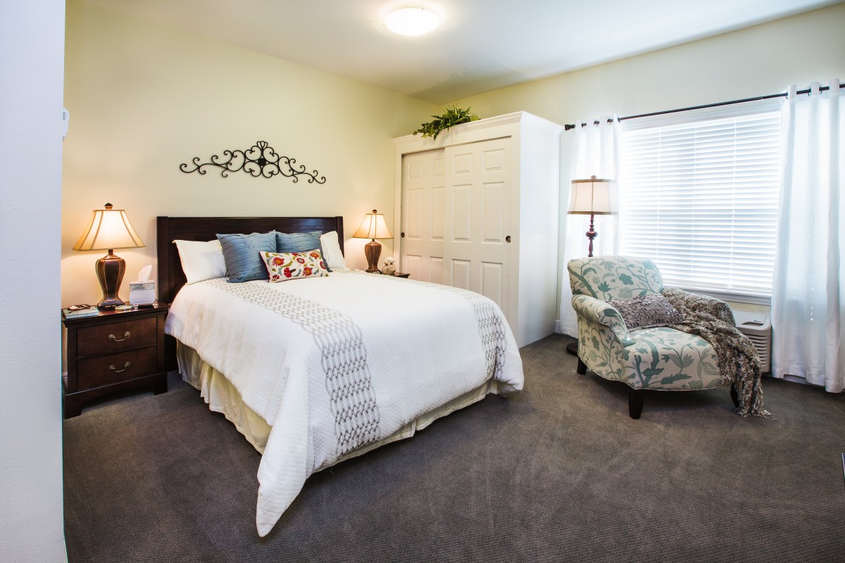 A cozy and well-decorated bedroom featuring a comfortable bed, a wardrobe, an armchair, and soft lighting.