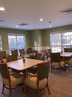 A well-lit dining room with several tables and chairs, featuring large windows that allow natural light to fill the space.
