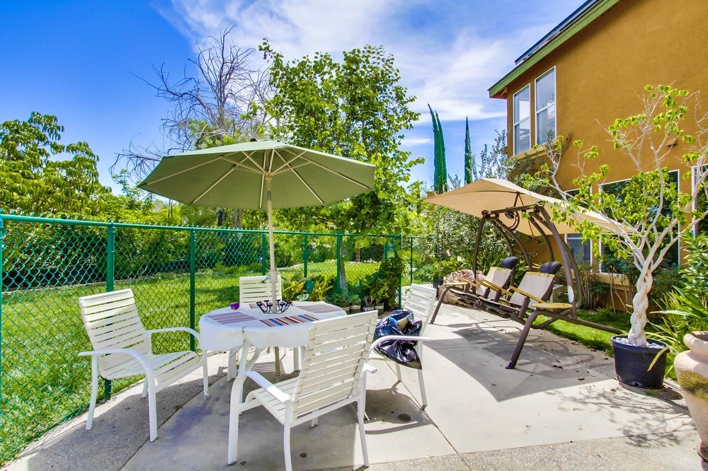 Sunny patio area with umbrella, chairs, and a garden swing.