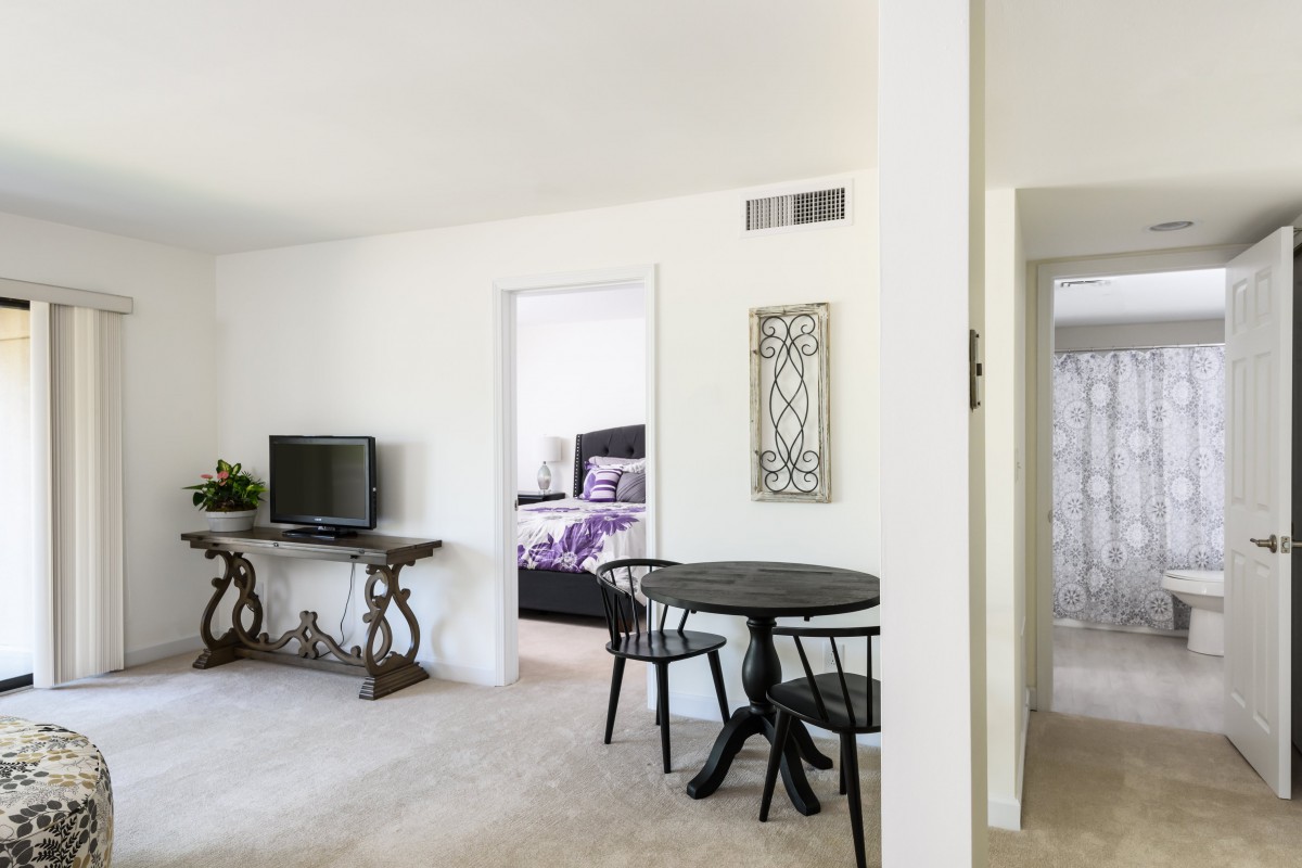 A cozy apartment interior featuring a living room with a TV, dining table with chairs, and a glimpse into the bedroom.
