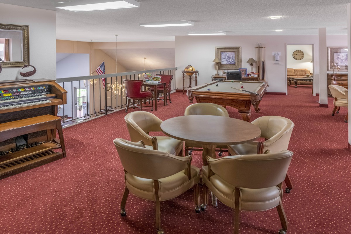 A cozy game room with a pool table and seating area on a red-carpeted floor.